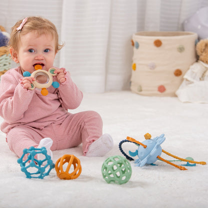 Baby chewing teething toy surrounded by colorful sensory toys on soft rug
