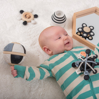 Happy baby on soft rug with sensory toys, teething ball, and developmental play items for infants