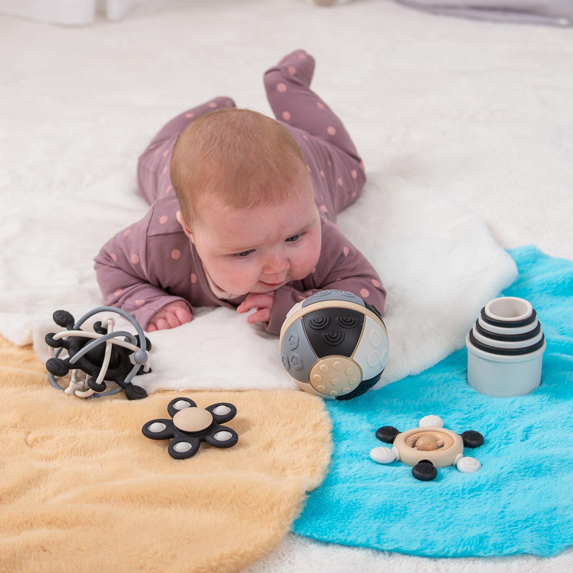 Baby playing with sensory toys on colorful play mat, featuring textured balls and stacking rings for early development.