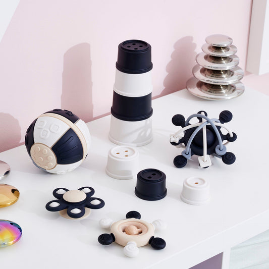 Modern baby sensory toys with stacking cups, textured balls, and fidget spinners on white table