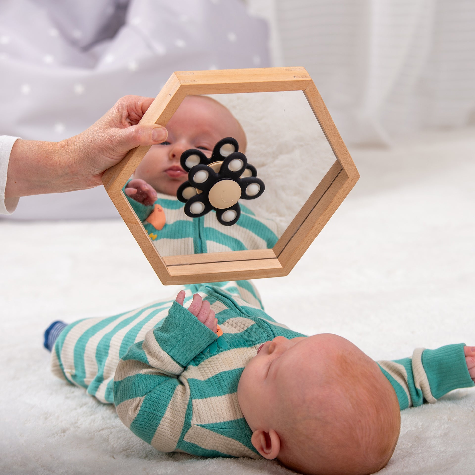 Baby looking at flower-shaped pop-it toy in wooden hexagon mirror, developmental sensory play for infants