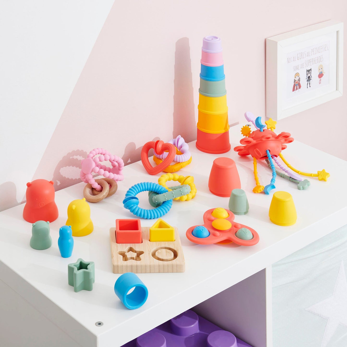 Colorful baby toys including stacking cups, teething rings, shape sorter, and sensory fidget spinner on white shelf