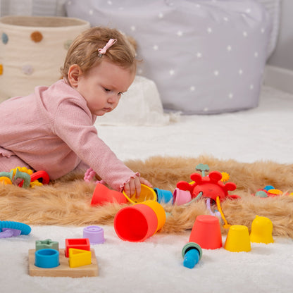 Baby playing with colorful stacking cups and shape sorter toys on soft rug