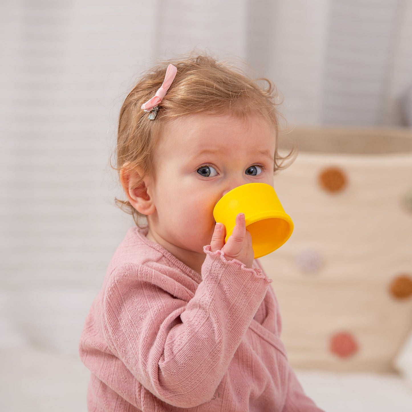 Toddler drinking from yellow sippy cup, wearing pink outfit and hair clip, ideal for baby feeding and playtime.
