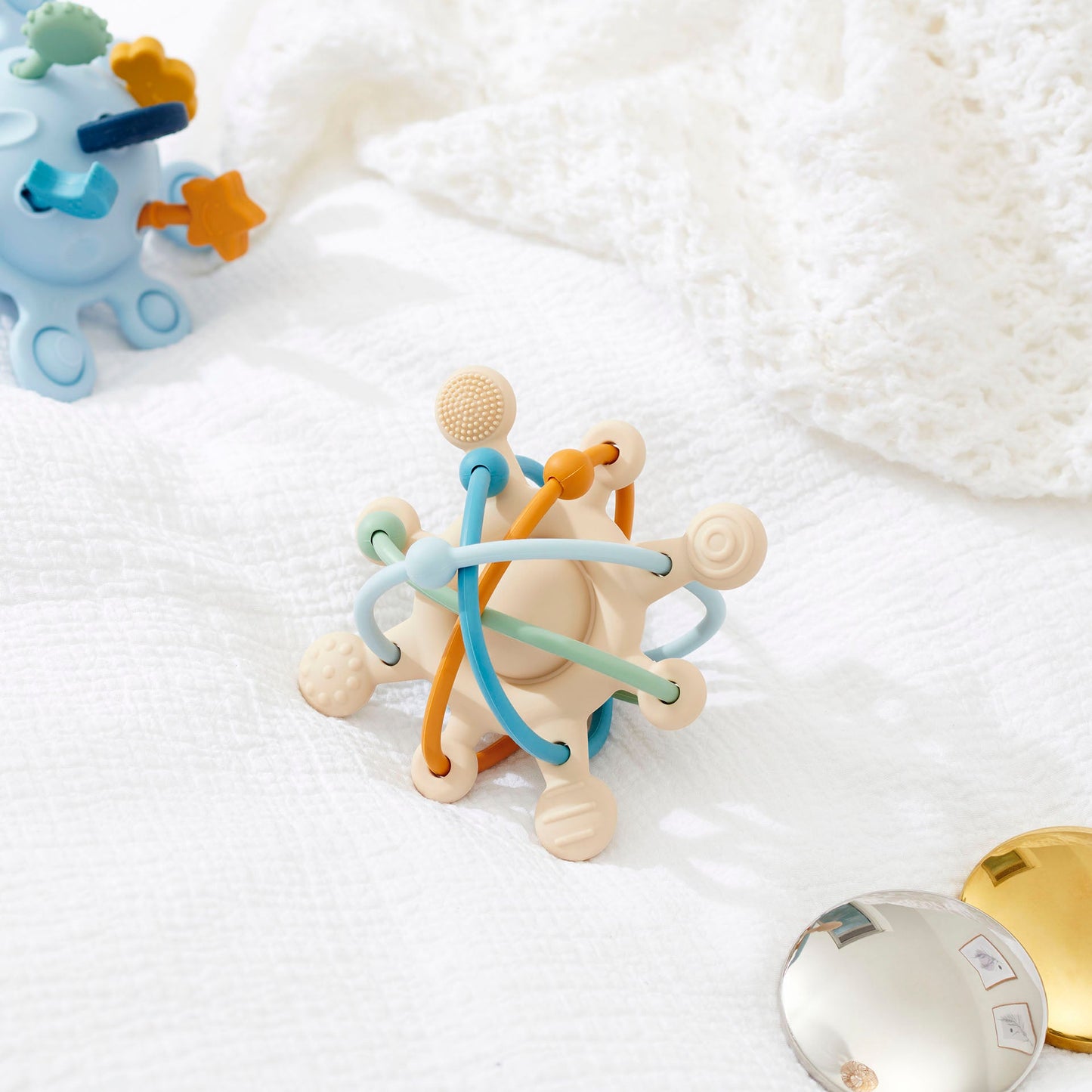 Colorful baby teether toy with textured beads and flexible rings on soft white blanket
