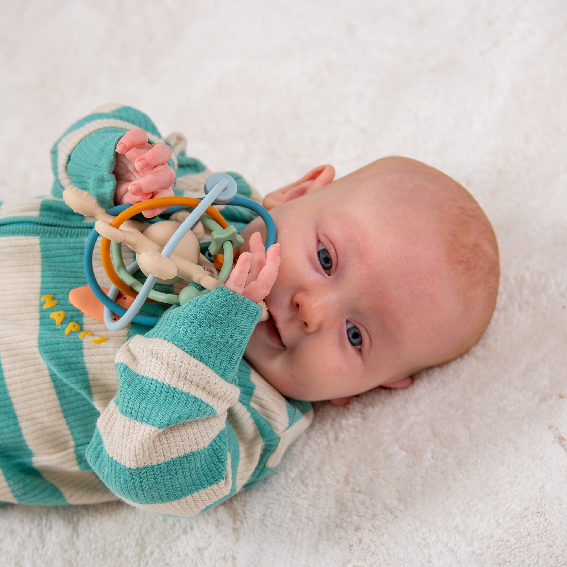 Baby playing with colorful sensory rattle toy on soft blanket