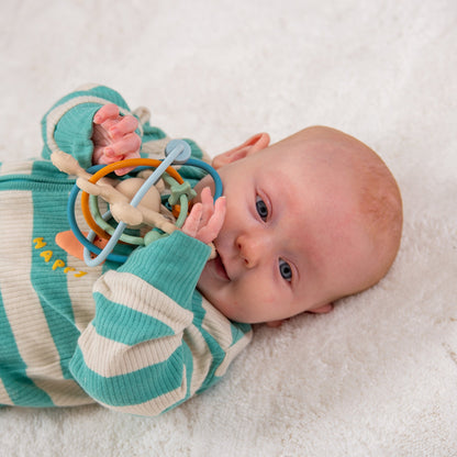 Baby playing with colorful sensory rattle toy on soft blanket