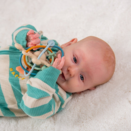 Baby playing with colorful sensory rattle toy on soft blanket