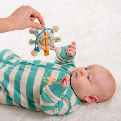 Baby in striped onesie playing with colorful sensory toy on soft white blanket