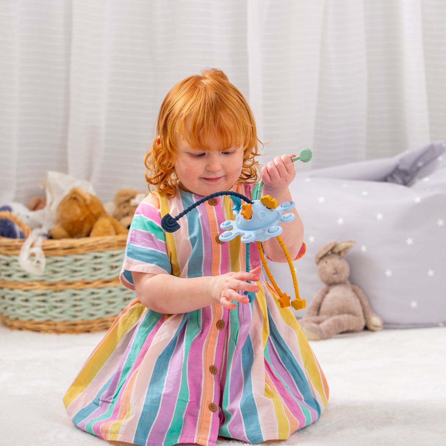 Toddler playing with colorful octopus sensory toy, rainbow dress, soft playroom setting