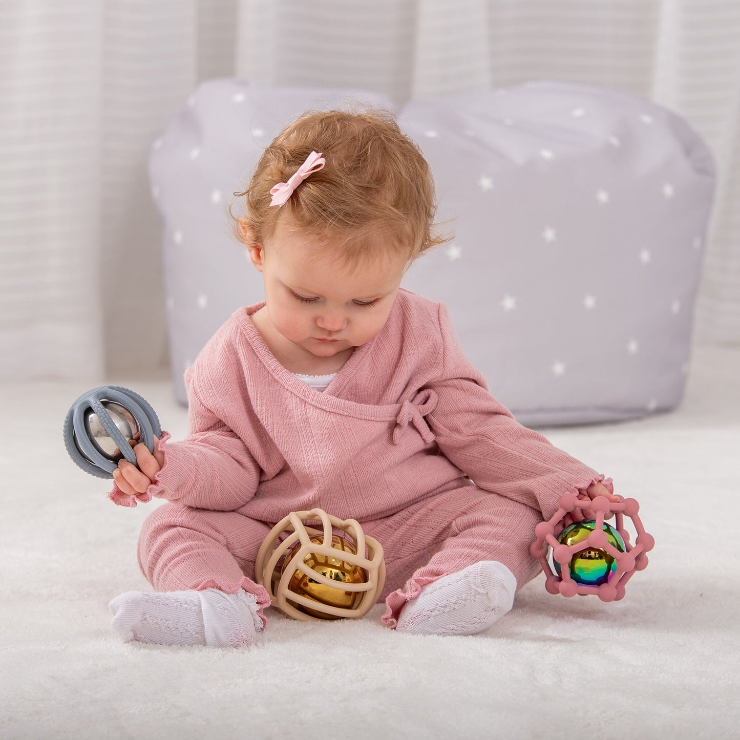 Baby playing with colorful sensory rattle toys on soft rug, developmental play for infants