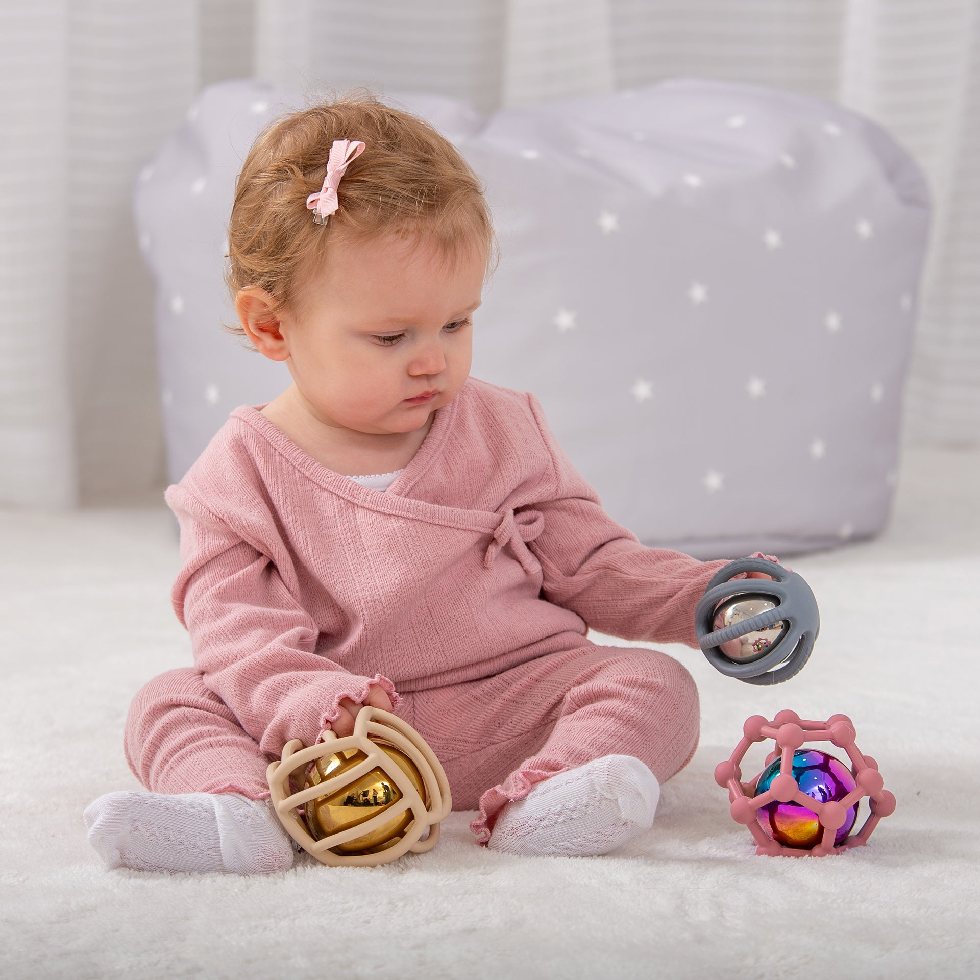 Baby playing with colorful sensory rattle toys on soft rug, developmental play for infants