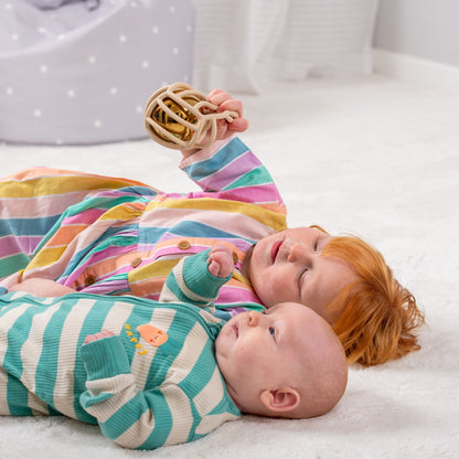 Baby and toddler playing with sensory rattle toy on soft rug, colorful striped outfits