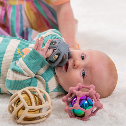 Baby chewing on gray teething toy with colorful sensory balls nearby