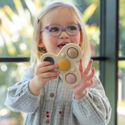 Child holding colorful fidget spinner toy with star and sun designs, wearing purple glasses