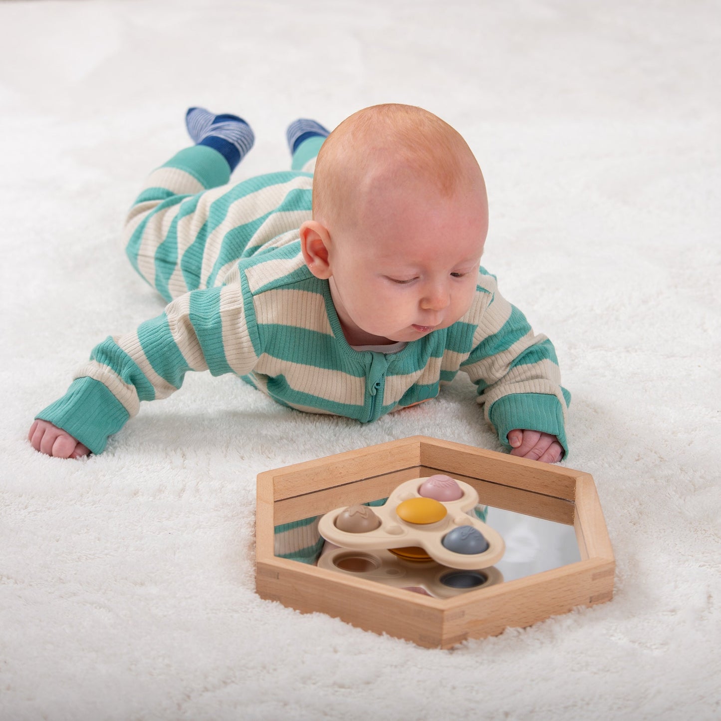 Baby playing with wooden sensory toy on soft white rug