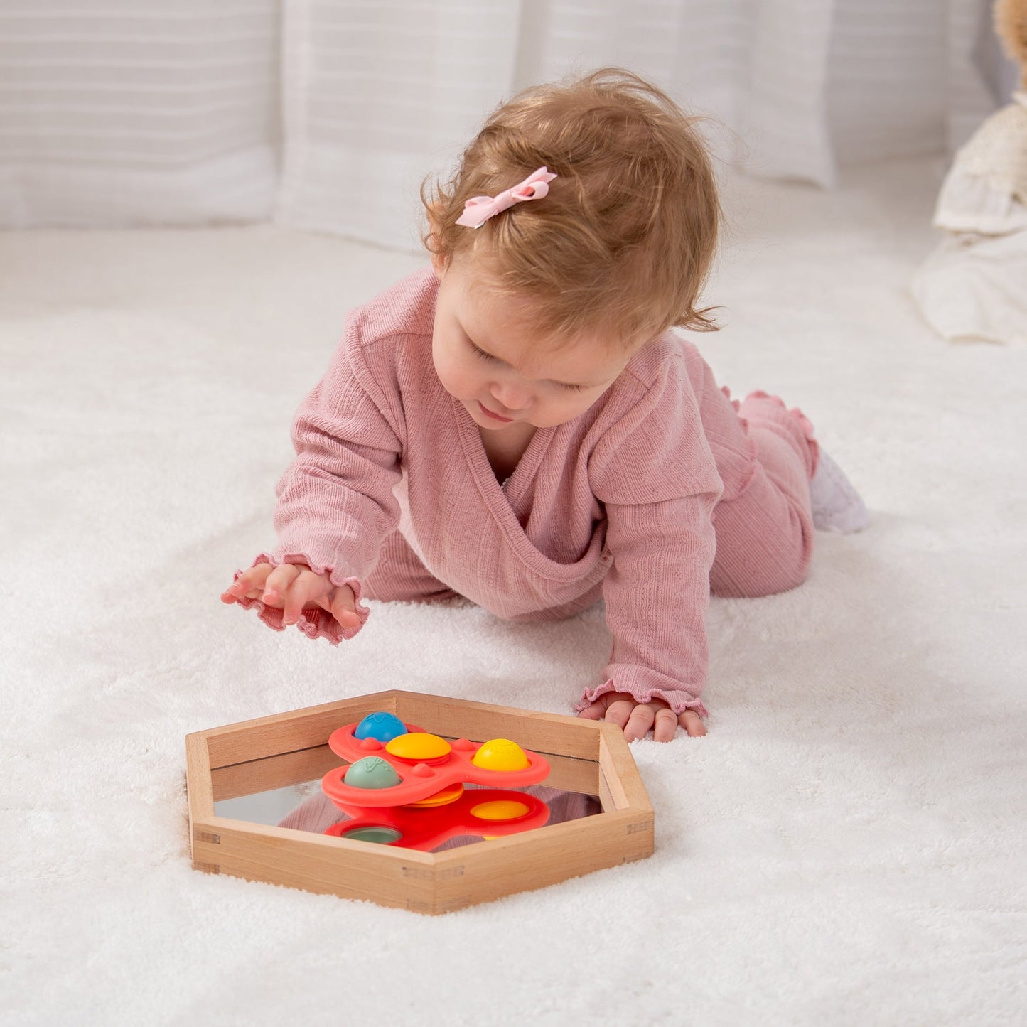 Baby playing with colorful sensory toy in wooden tray on soft rug