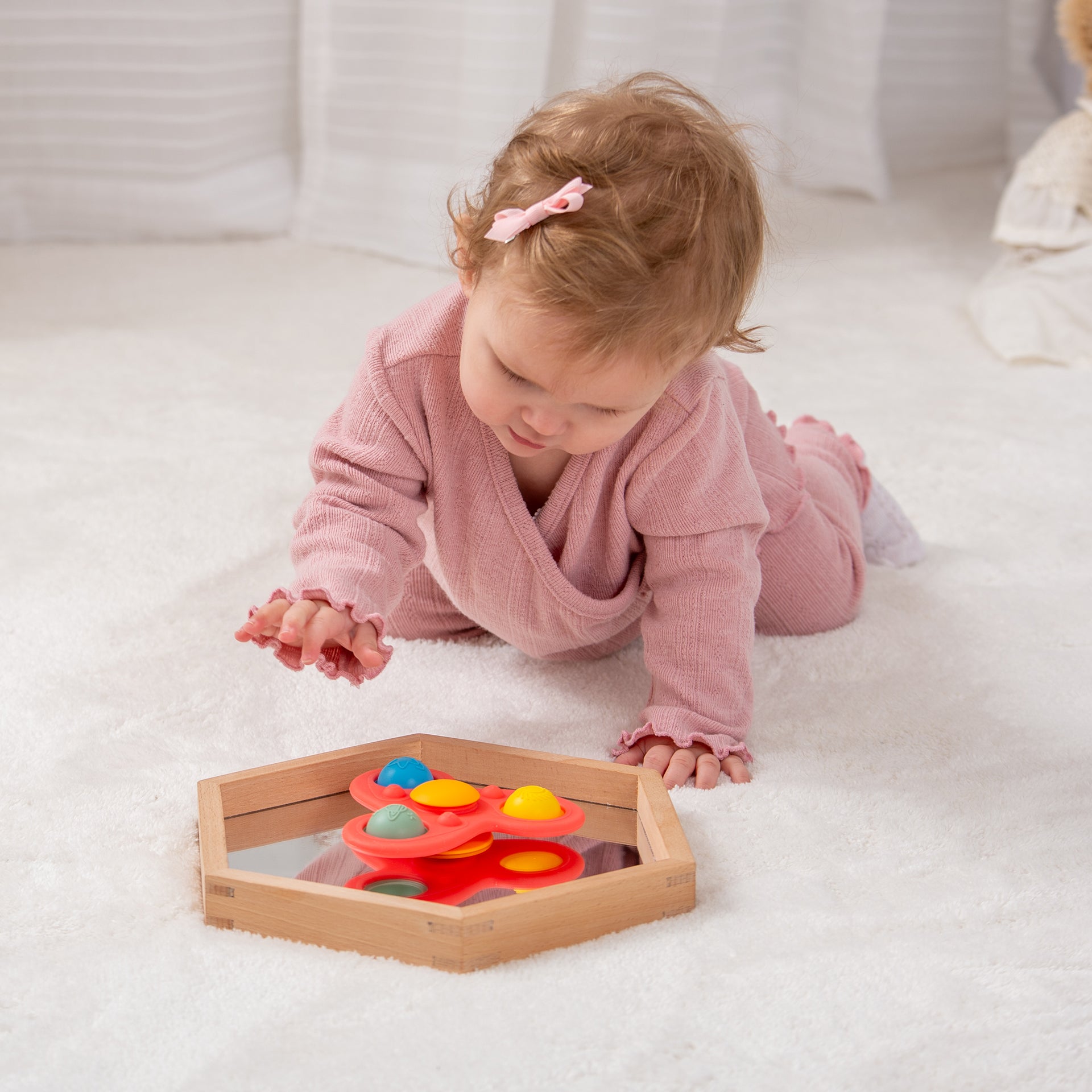 Baby playing with colorful sensory toy in wooden tray on soft rug
