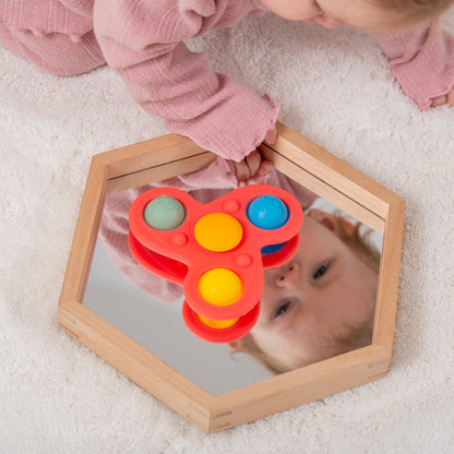Baby playing with red pop-it toy on wooden mirror, sensory development activity
