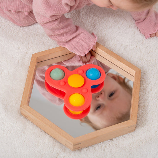 Baby playing with red pop-it toy on wooden mirror, sensory development activity