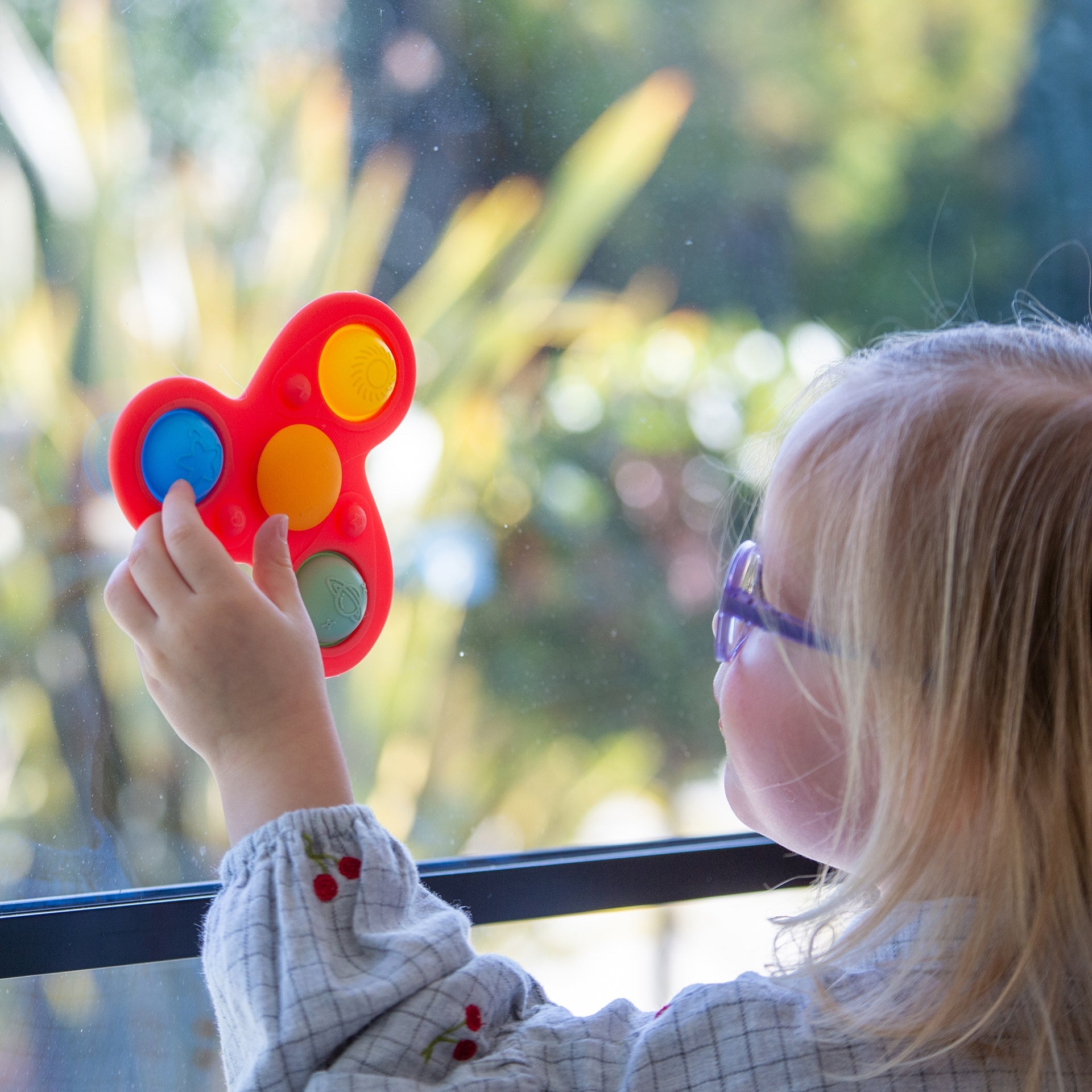 Child playing with red fidget toy featuring colorful buttons near window
