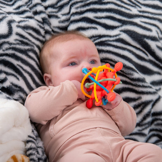 Baby chewing colorful teething toy on zebra print blanket, ideal for infant sensory play and development.