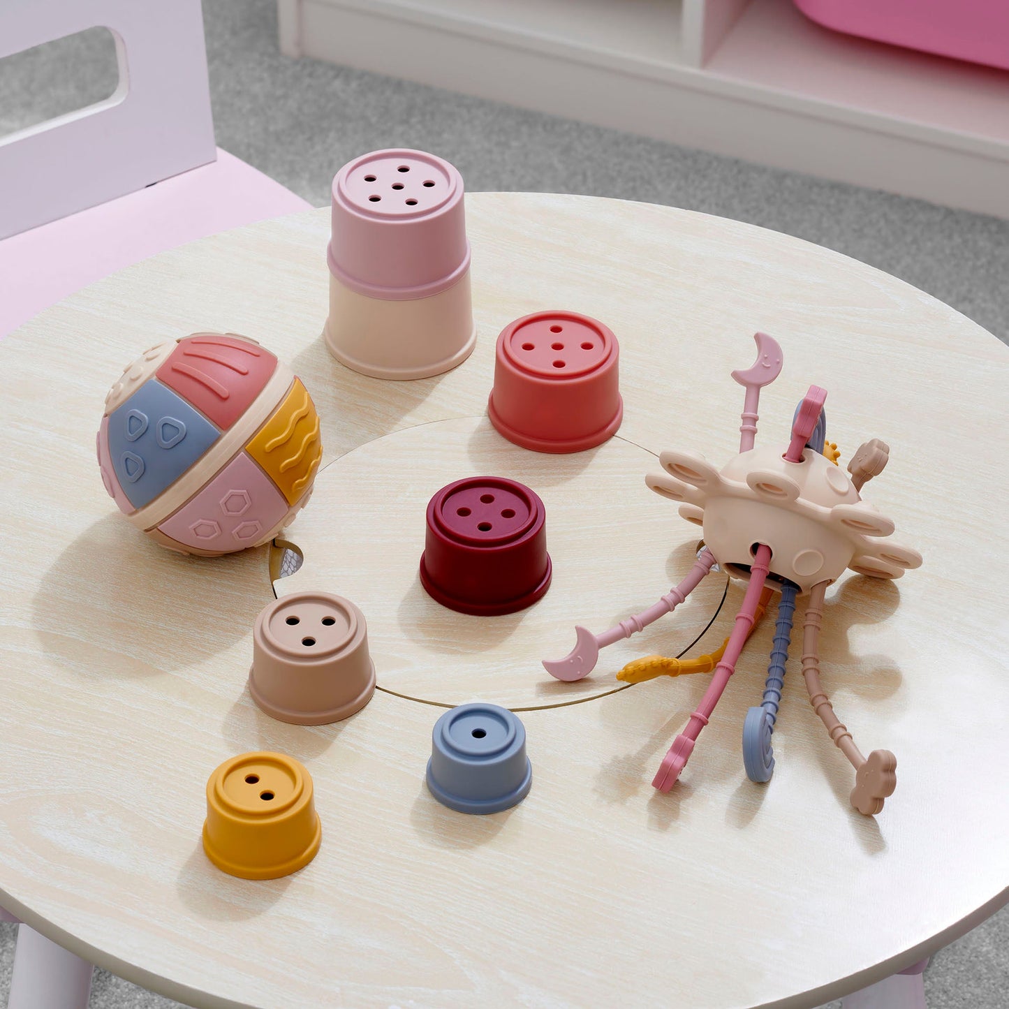 Colorful toddler toys including stacking cups, textured ball, and sensory activity toy on wooden table