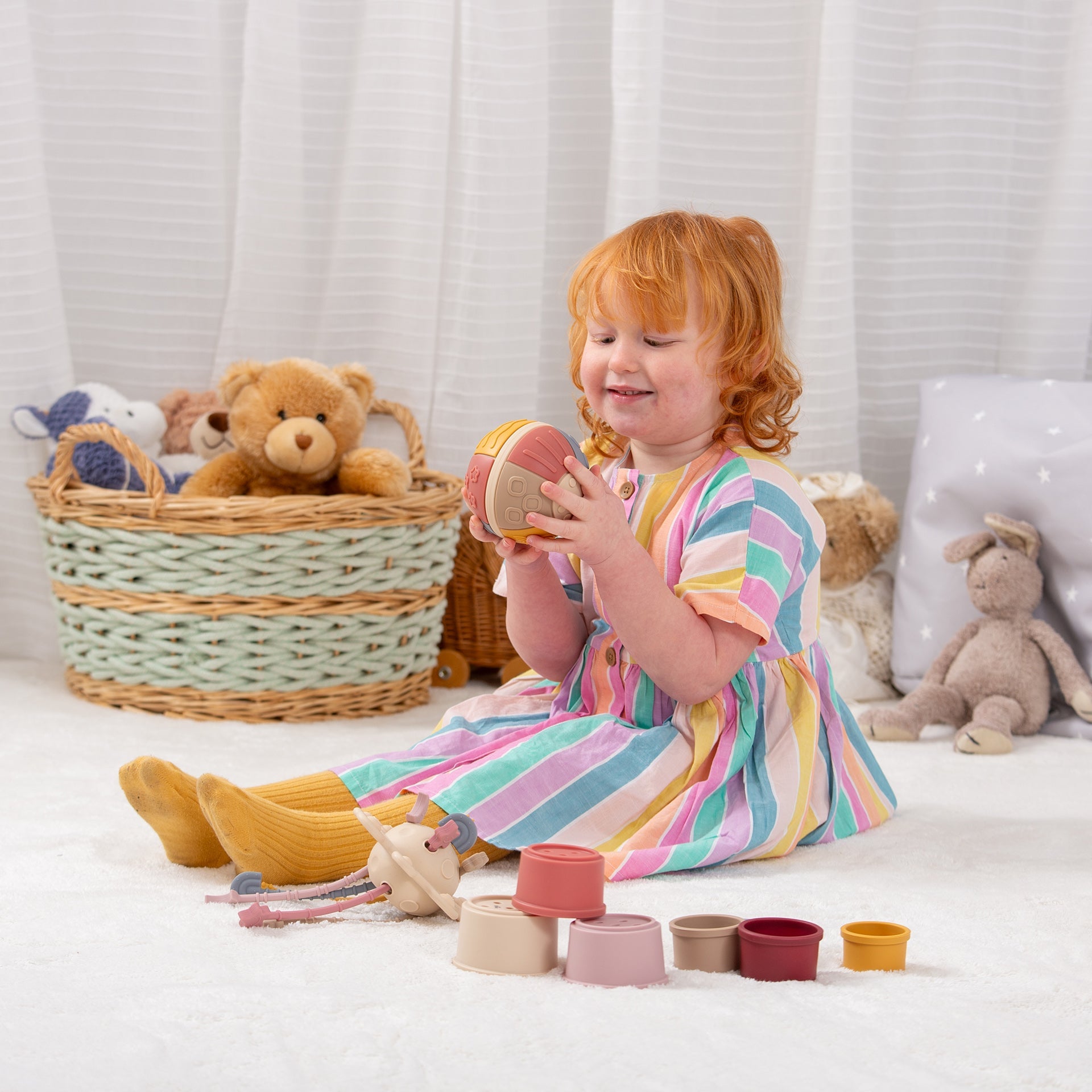 Child playing with colorful stacking toys and soft teddy bears in a cozy playroom setting