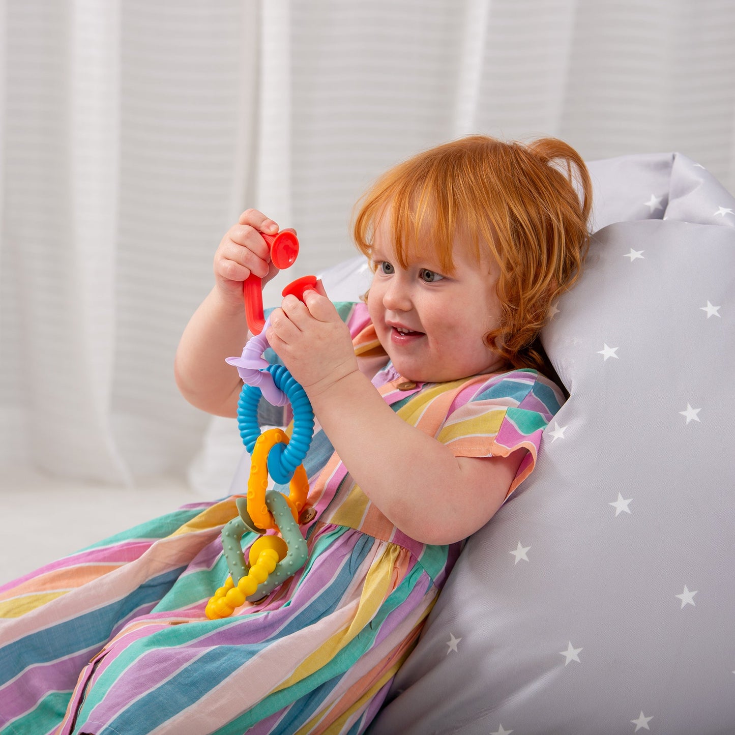 Child playing with colorful sensory teething toy on star-patterned cushion