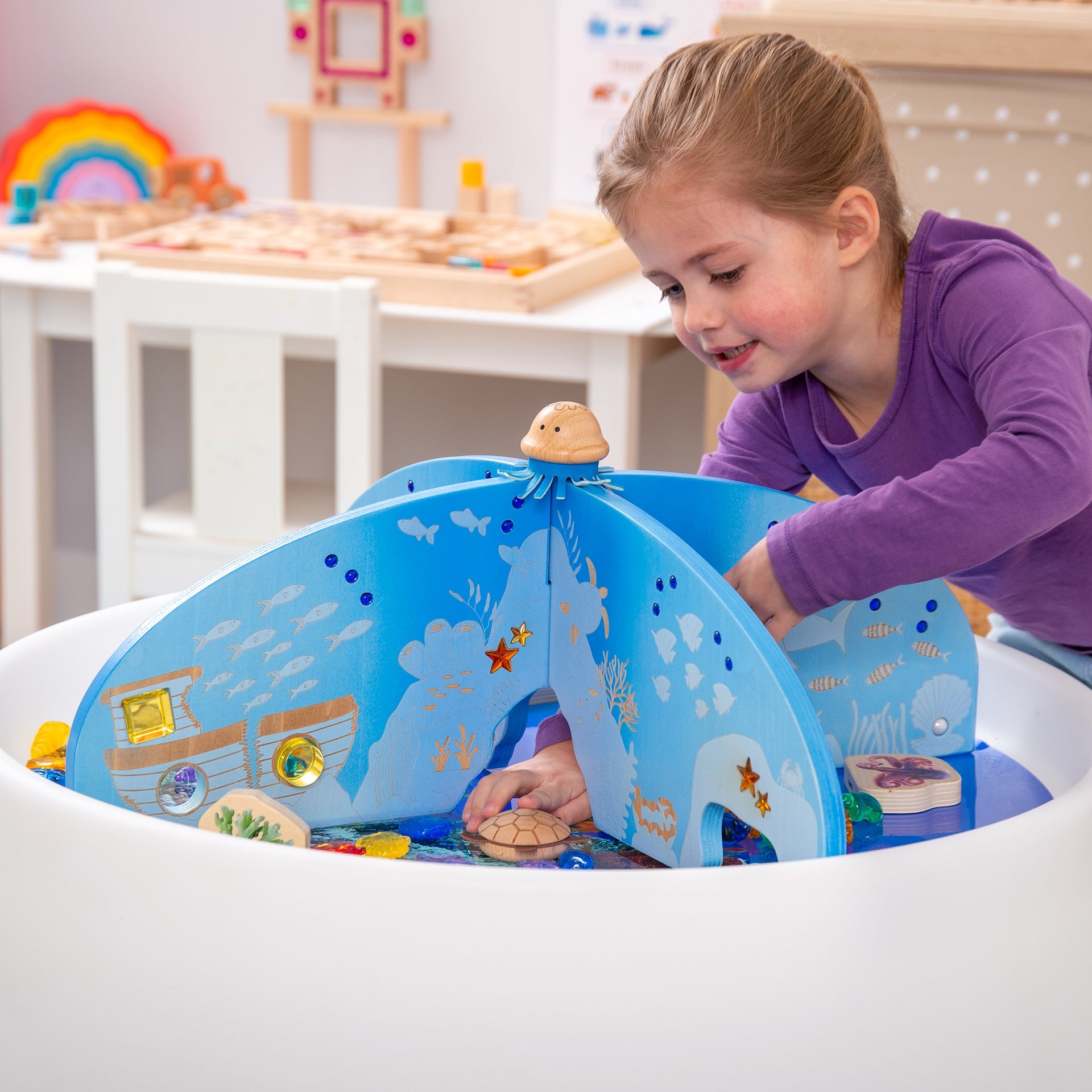 Child playing with wooden ocean-themed sensory water table featuring sea creatures and underwater scenes