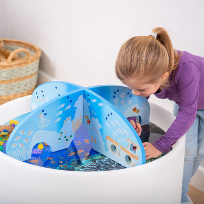 Child playing with ocean-themed wooden toy set in sensory bin, featuring sea creatures and underwater scenes.