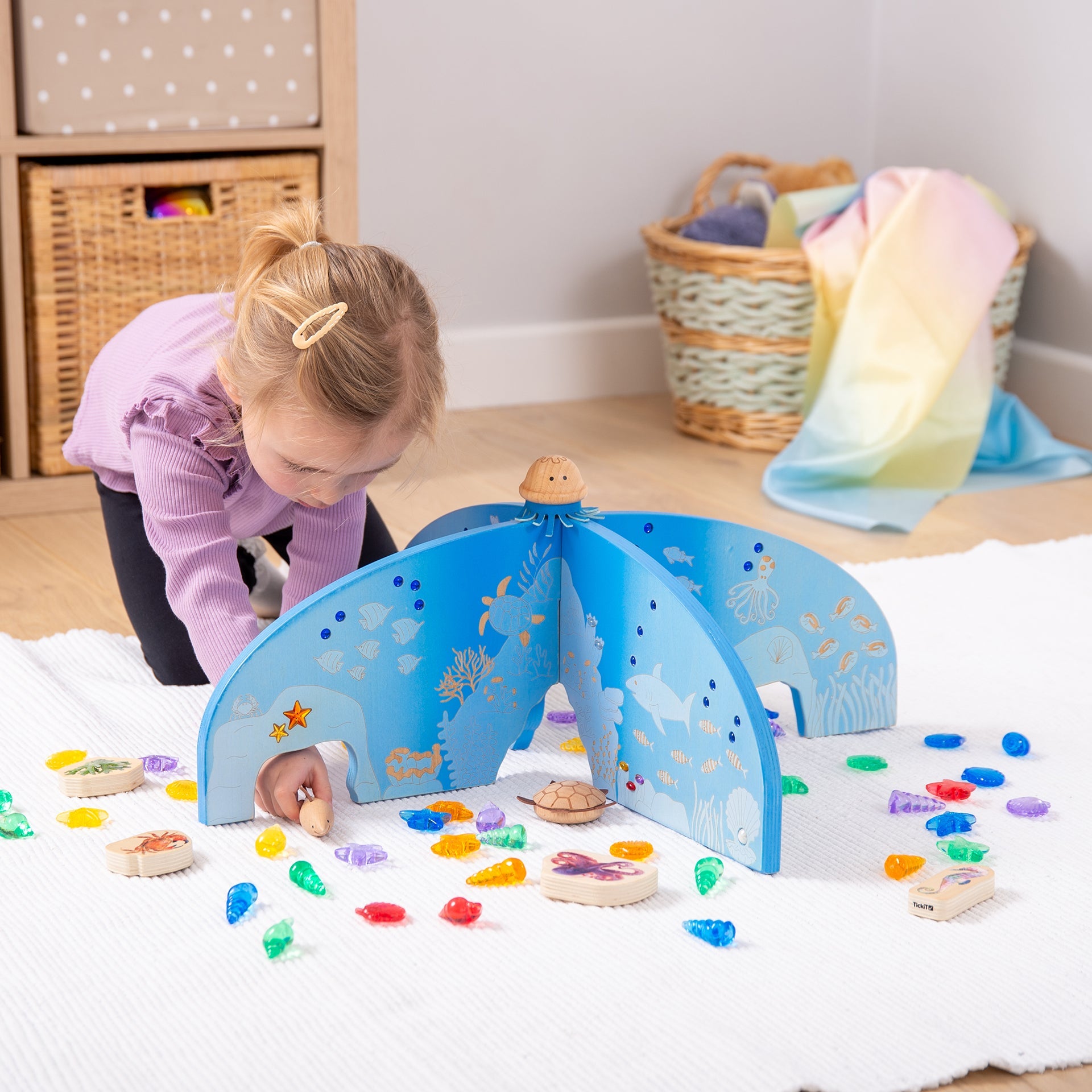 Child playing with wooden ocean-themed toy set featuring sea creatures and colorful gems on a white rug