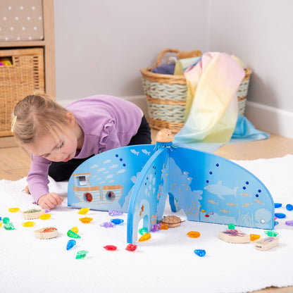 Child playing with wooden ocean-themed toy set featuring sea creatures and colorful gems on white rug
